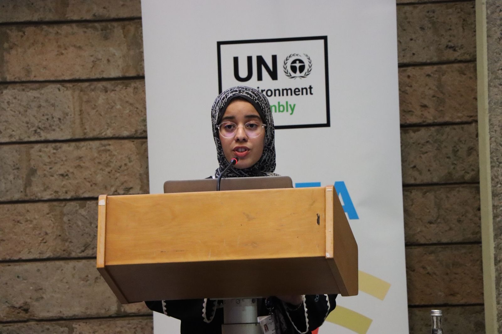 Oumnia wearing a patterned hijab and speaking at the UNEA podium